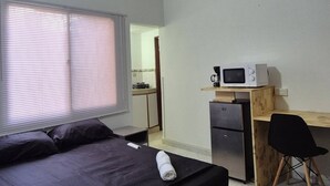 A bedroom with a bed, a desk with a computer and a microwave, and a kitchenette in the background. - Studio 3 Paisible 5 Minutes From El Rodadero Beach (Santa Marta)