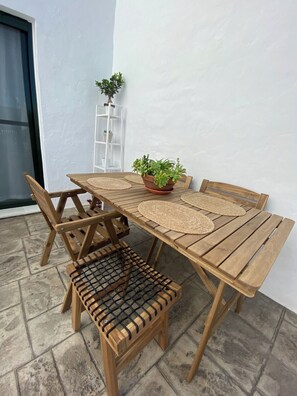 Una mesa de madera con individuales tejidos, un banco y una planta en maceta.
