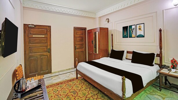 A hotel room with a large bed, wooden wardrobe, a flat-screen TV, and a bedside table with a vase of flowers. - Palette Hotel and Resorts Jodhpur (Jodhpur)