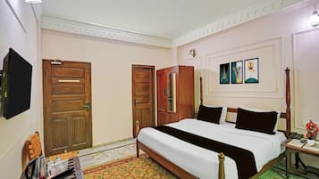 A hotel room with a large bed, wooden wardrobe, a flat-screen TV, and a bedside table with a vase of flowers.