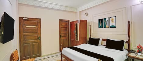 A hotel room with a large bed, wooden wardrobe, a flat-screen TV, and a bedside table with a vase of flowers.