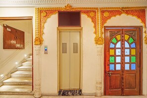 Un ascensor, una puerta de madera con vidrieras y una escalera.