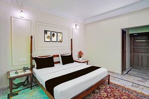 A neatly arranged bedroom with a bed, bedside tables, a wall-mounted light fixture, and a door. - Palette Hotel and Resorts Jodhpur (Jodhpur)