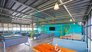 Ein modernes Restaurantambiente mit hohen Decken, freiliegenden Balken und einer Mischung aus Sitzgelegenheiten, darunter Essecken und Tische.