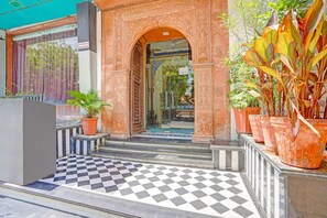 Fachada de un hotel con un arco ornamentado, suelo a cuadros y plantas en macetas.