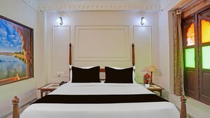 Ein Hotelzimmer mit einem großen Bett, zwei Nachttischen, einem Schreibtisch, einem Bild an der Wand, einem Fenster mit Vorhängen und einer Tür mit Buntglasdekor.