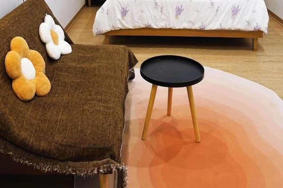A bedroom with a bed, a chair, a small table, and wall art.