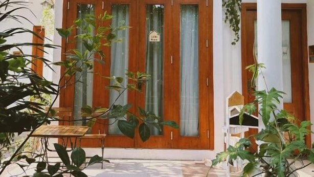 A building entrance with a wooden door, a sign, and a staircase leading up. - In Home (Hanoi)