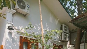 A white building with a wooden door, a small table with a checkered tablecloth, and a white picket fence. - In Home (Hanoi)
