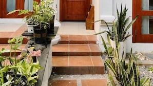 A front entrance with a wooden door, potted plants, and a tiled staircase leading to the door. - In Home (Hanoi)