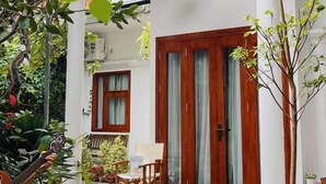 A covered porch with a wooden door, two hanging wicker lamps, and a potted plant. - In Home (Hanoi)