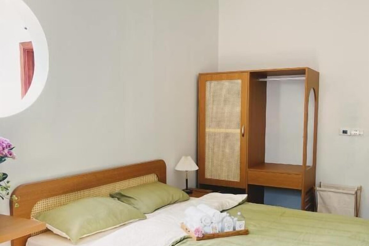 A single bed with a wooden frame, a green bedspread, and a wooden wardrobe with a wicker door.