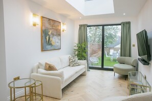 Ein modernes Wohnzimmer mit einer Couch, einem Sessel, einem Glastisch und einem Gemälde an der Wand.