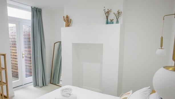 Une chambre à coucher avec un lit, un miroir, une cheminée et une fenêtre avec des rideaux.