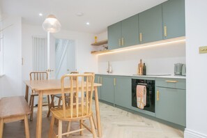 A modern kitchen with a dining area, featuring wooden furniture, a pendant light, and teal cabinetry. - Three bedroom  in United Kingdom of Great Britain and Northern Ireland, Brighton and Hove (Brighton and Hove)