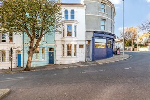 A street view with a row of buildings, including a corner house with a bay window and a blue door. - ✨ Stylish 3-Bed Victorian Maisonette in Queens Park (Brighton and Hove)