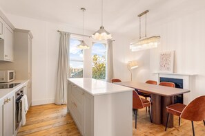 A modern kitchen with a central island, wooden flooring, and a dining area with chairs. - ✨ Stylish 3-Bed Victorian Maisonette in Queens Park (Brighton and Hove)