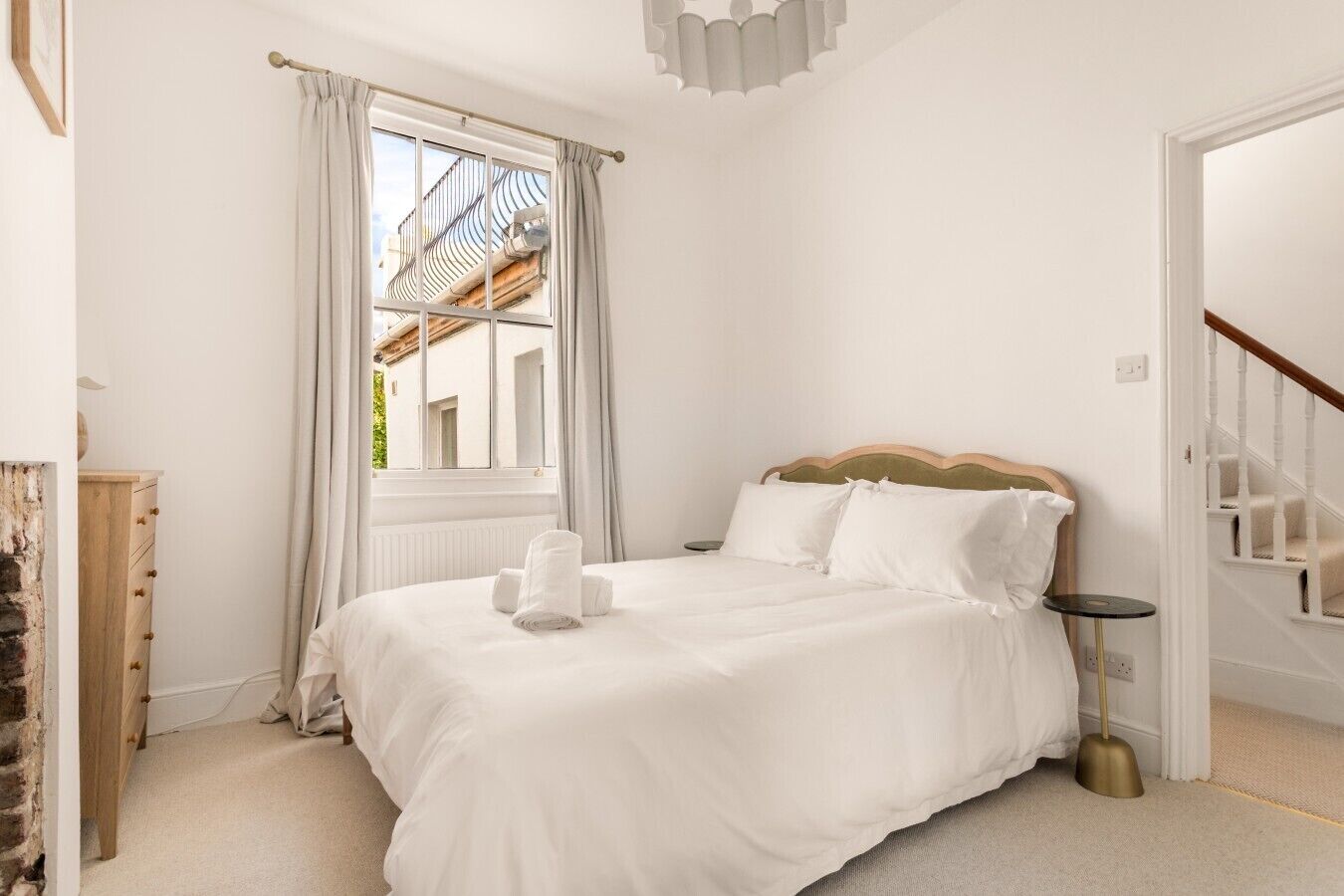 Ein Schlafzimmer mit einem Bett, einem Fenster mit Vorhängen, einer Holzkommode und einer Treppe.