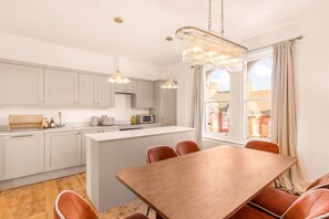 A modern kitchen with white cabinets, a wooden dining table, and a chandelier. - ✨ Stylish 3-Bed Victorian Maisonette in Queens Park (Brighton and Hove)