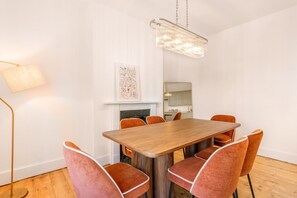 Ein Essbereich mit einem Holztisch, sechs orangefarbenen Stühlen, einer Pendelleuchte, einem Wandbild und einer Stehlampe.