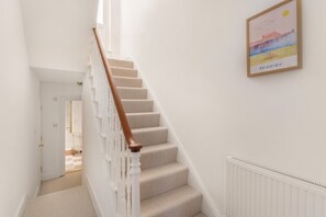 Eine Treppe mit hölzernem Geländer und beige gefärbten Stufen führt zu einem Raum mit einer weißen Heizung.