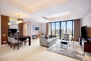 A modern living room with a dining area, a sofa, a TV, and large windows offering a city view.