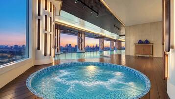 A modern indoor swimming pool with a city view, wooden flooring, and contemporary design elements.