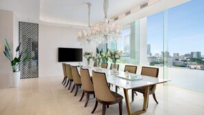 A modern dining room with a large table, chairs, a chandelier, and a TV on the wall. - Vasa Suite Surabaya (Surabaya)