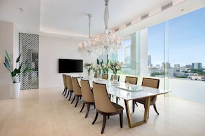 A modern dining room with a large table, chairs, a chandelier, and a TV on the wall.