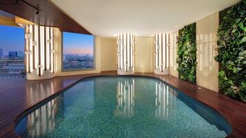 Ein moderner, überdachter Pool mit Blick auf die Stadt, einem Holzboden und einer grünen Wand mit Pflanzen.