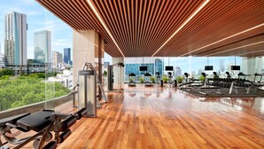 A gym with exercise equipment, large windows, and a city view. - Vasa Suite Surabaya (Surabaya)