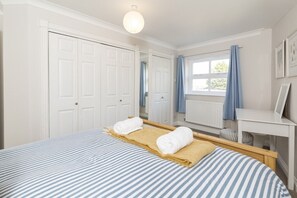A bedroom with a bed, a desk, a window with curtains, and a radiator.