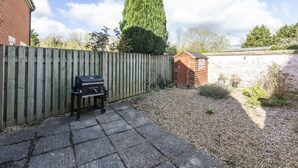 Ein Garten mit Holzzaun, Grill und Gartenhaus.