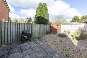 A backyard with a wooden fence, a barbecue grill, and a shed.
