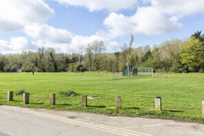 A grassy field with a fence, a small structure, and trees in the background.