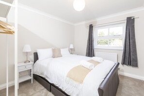 A bedroom with a bed, bedside tables, a window with curtains, and a radiator.