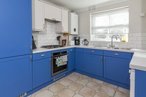 A kitchen with blue cabinets, a gas stove, a built-in oven, and a window with blinds.