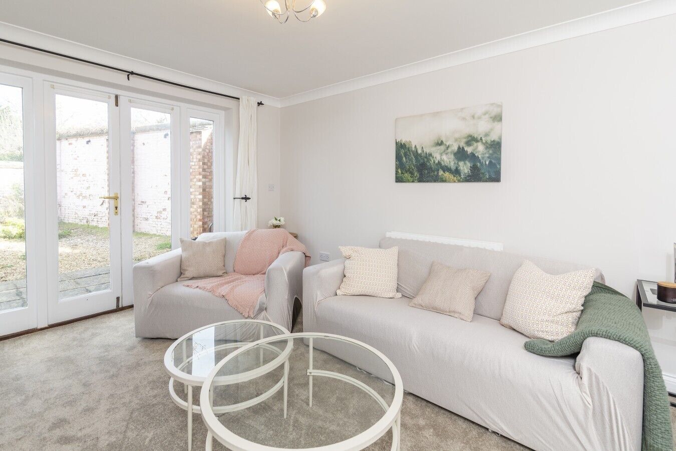 Een woonkamer met een bank, twee stoelen, een glazen salontafel en een schilderij aan de muur.