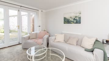 Een woonkamer met een bank, twee stoelen, een glazen salontafel en een schilderij aan de muur.
