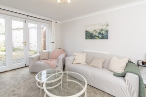 Una sala de estar con un sofá, dos sillones, una mesa de centro de vidrio y un cuadro en la pared.