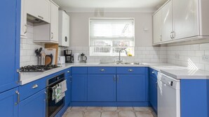 Eine Küche mit blauen Schränken, einem Gasherd, einem Geschirrspüler und einem Fenster mit Jalousien.