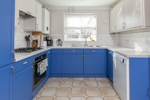 A kitchen with blue cabinets, a gas stove, a dishwasher, and a window with blinds.