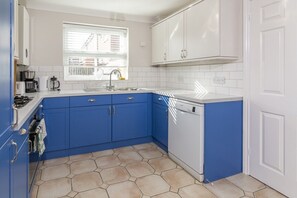 Una cocina con armarios azules, un lavavajillas blanco y una ventana con persianas.
