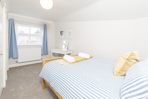 A bedroom with a bed, a bedside table, a window with curtains, and a radiator.