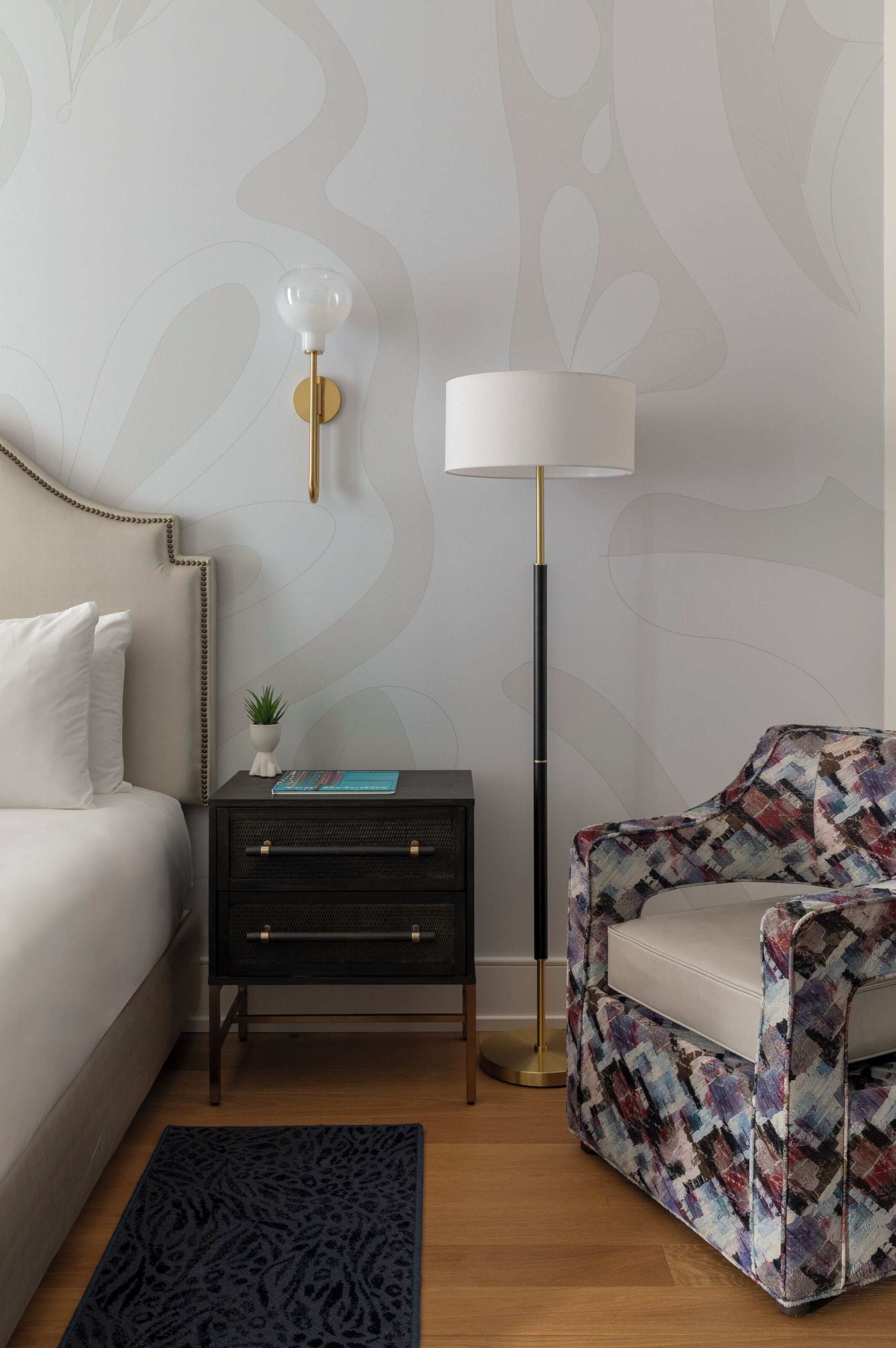 A bedroom with a bed, a nightstand, a lamp, a chair, and a patterned rug.