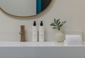 A bathroom with a white sink, two white bottles labeled 'CULTI,' a gold faucet, a white vase with green leaves, and a white towel on a white tray. - The Monarch Hotel, HQ Collection New Orleans (New Orleans)