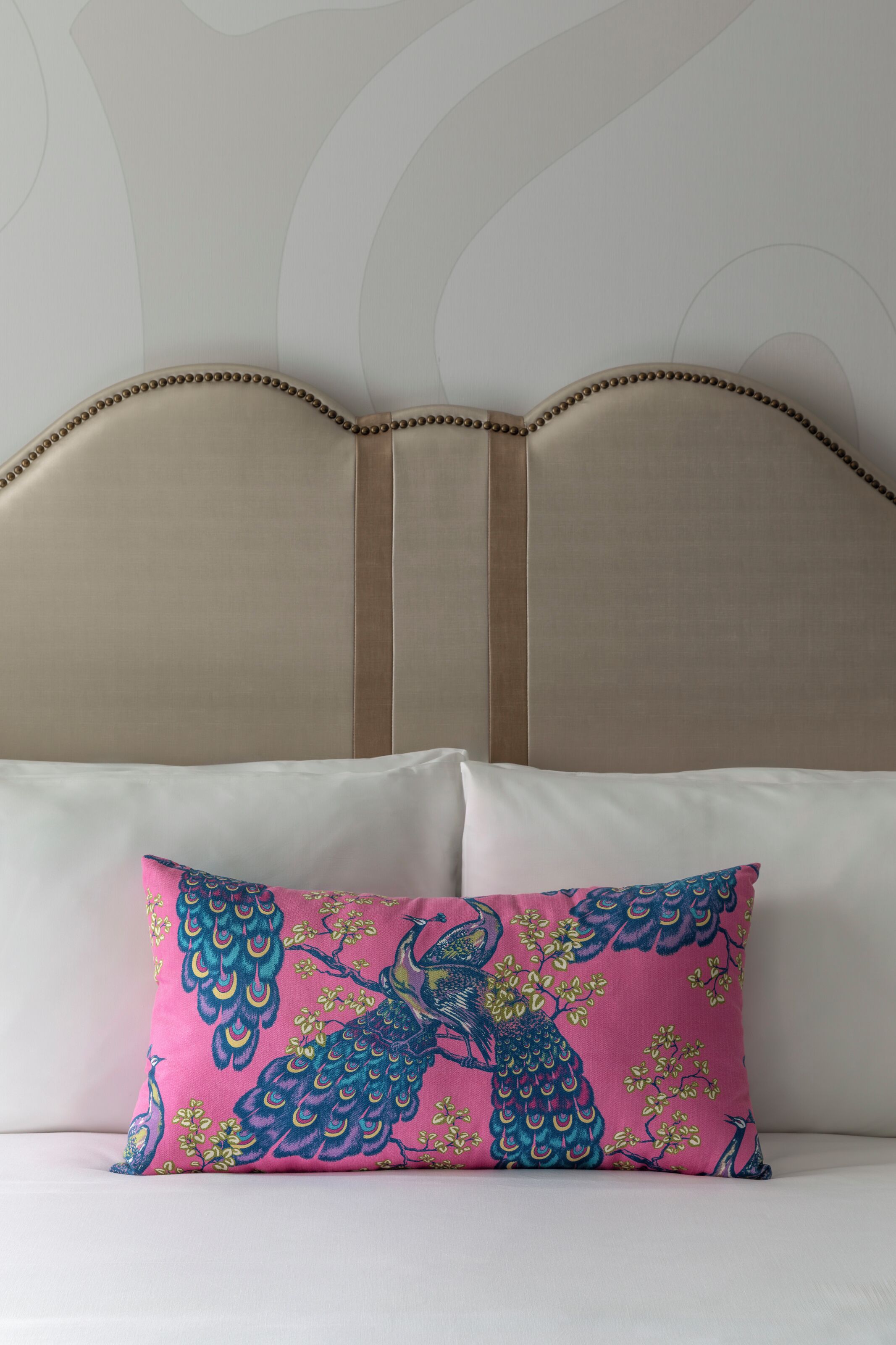 Una cama con cabecera, almohada blanca y cojín decorativo con diseño de pavo real.