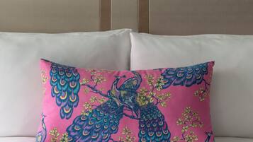 Una cama con cabecera, almohada blanca y cojín decorativo con diseño de pavo real.