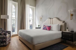 A hotel room with a large bed, a chair, a nightstand, and a window with curtains.