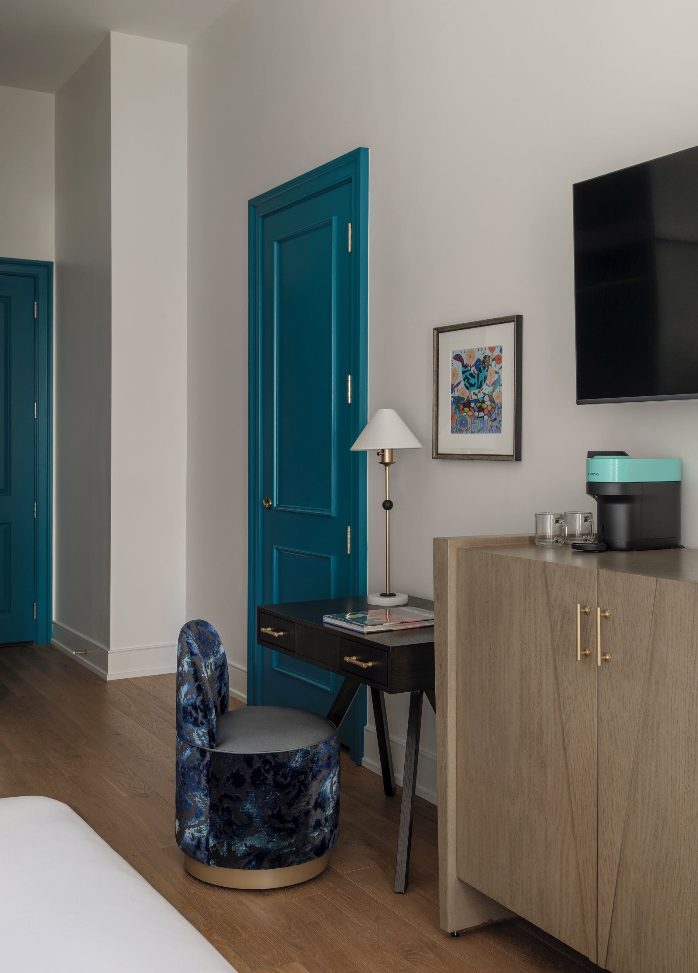 Een hotelkamer met een blauwgroene deur, een bureau met lamp, een televisie en een kast.